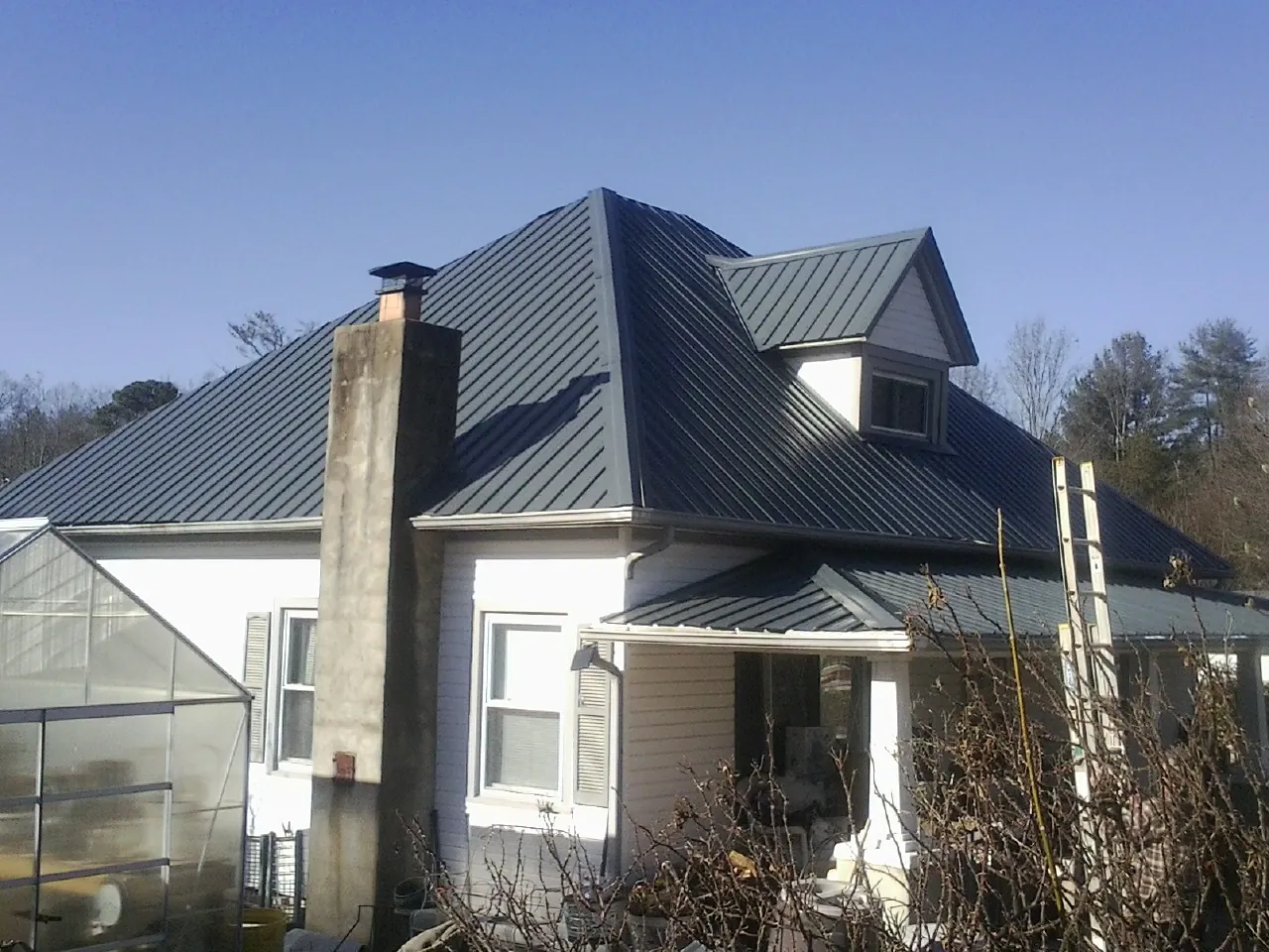 Dark blue standing seam metal roof on a white farmhouse with dormer — Slate & Tile Roof Repair by Roofing Brothers in Phelps