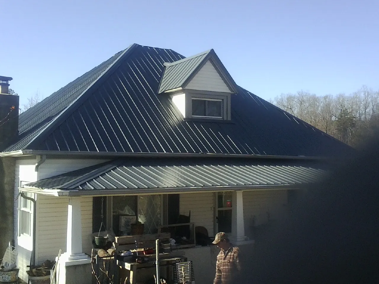 Dark blue standing seam metal roof with a dormer above a front porch in Phelps