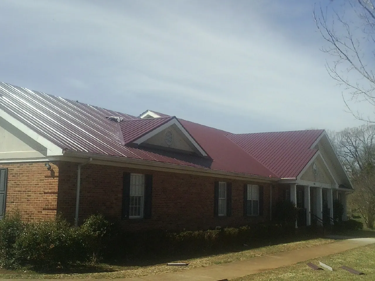 Red metal roof with gabled entries on a long brick building, from a Hail Damage Roof Repair job in Phelps