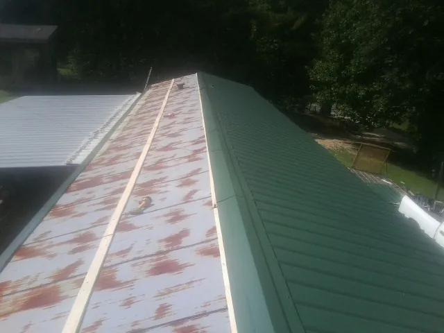 Old rusted panels beside newly installed green metal roofing — Wind Damage Roof Repair by Roofing Brothers in Phelps
