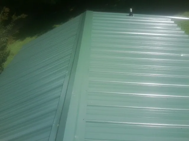 New green metal panels meeting at the ridge of a roof — Flat Roof Repair work by our crew in Phelps