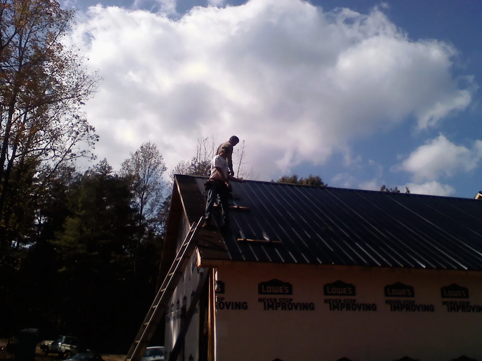 Roofer fastening dark metal panels high against a cloudy sky, from a Roof Inspection job in Phelps