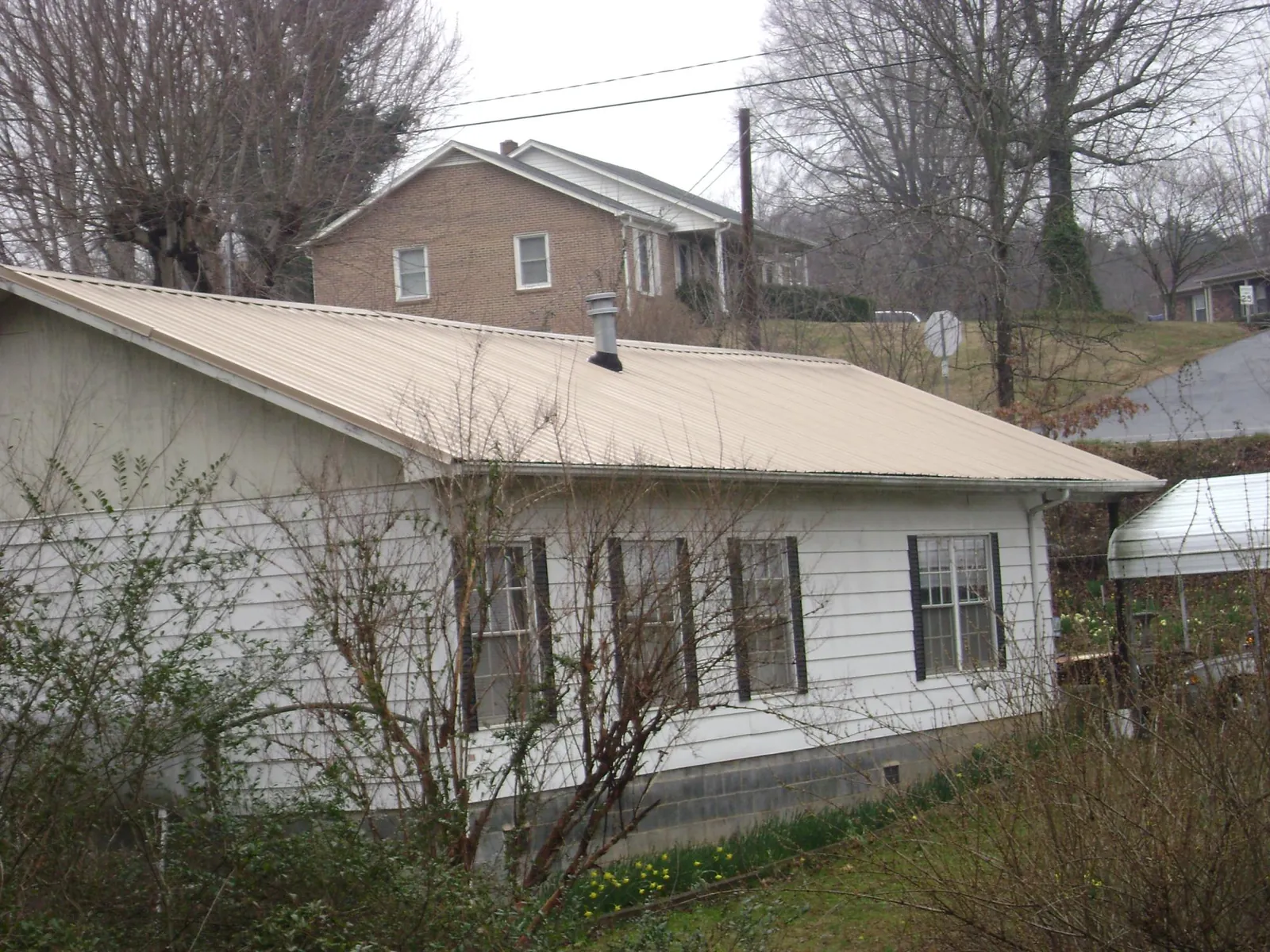 Tan metal roof on a white sided house set into a hillside — Commercial Roofing by Roofing Brothers in Phelps