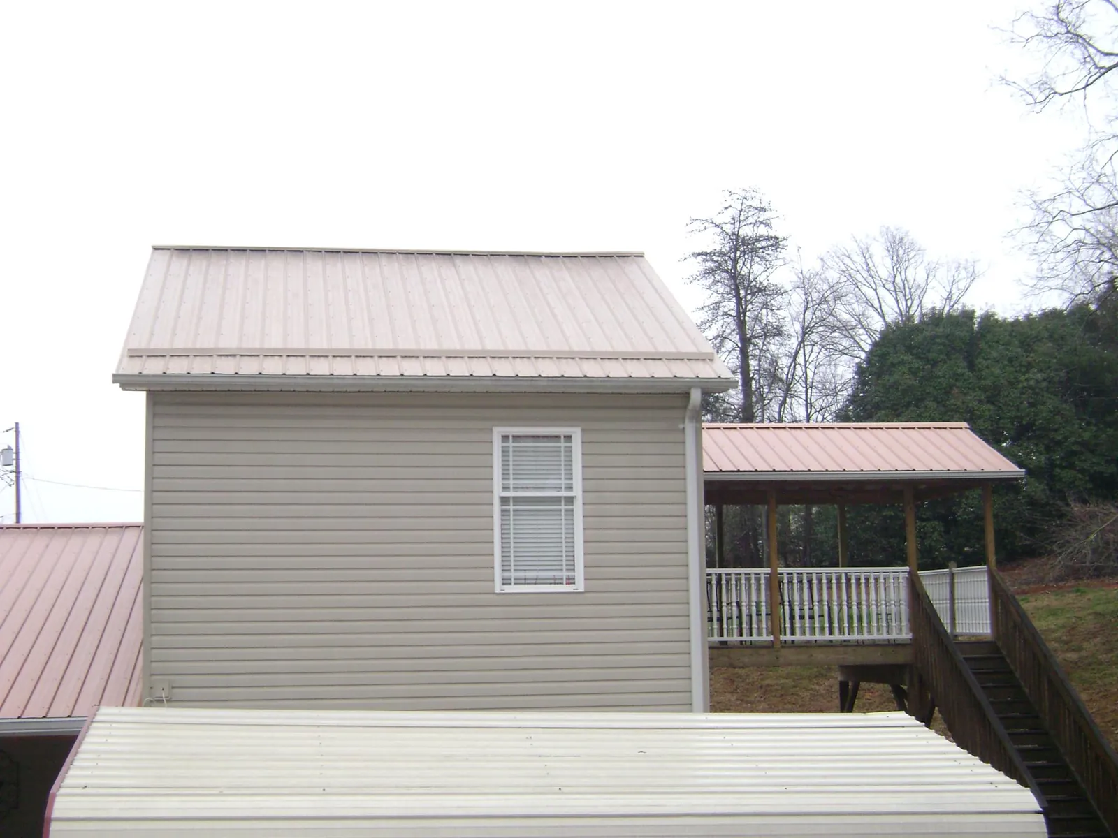 Tan metal roofs on a two story addition and attached porch, from a Roof Replacement job in Phelps
